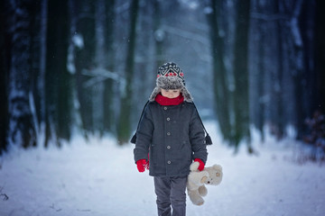 Sad lost child, boy in a forest with teddy bear, wintertime