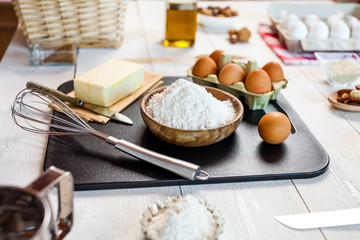 Baking ingredients in rural kitchen - dough recipe ingredients (eggs, flour, milk, butter, sugar) and rolling pin on wooden white table.