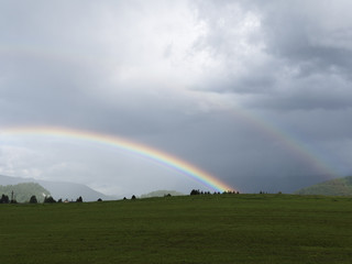 Alpine landscape with beautiful rainbow. Mountains, meadows and pastures. Rainy weather. Idyllic virgin and clean landscape. Salzburg vacation landscape. Mystical foggy evening scene with sun bow.