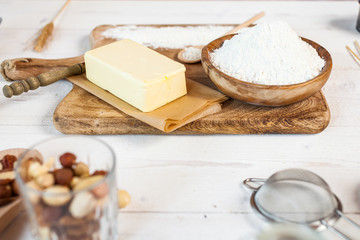 Baking ingredients in rural kitchen - dough recipe ingredients (eggs, flour, milk, butter, sugar) and rolling pin on wooden white table.