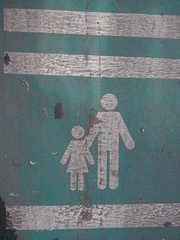 Old peeled white painted parent and child icon traffic sign on green road floor