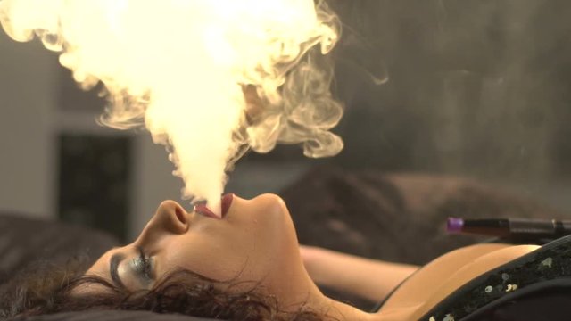 Attractive woman is having the rest while smoking the hookah and laying on the black sofa. Close-up side view.