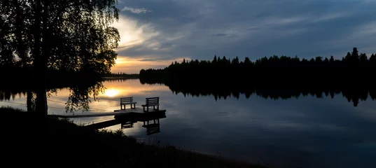 Gordijnen Empty footbridge with a bench on a lake in Lapland. Midnight sun in summertime. © tommitt