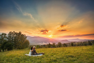 nature and people concept - happy loving couple sitting on plaid in field. background mountain