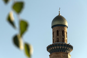 Obraz premium Moslem minaret of a mosque against a blue sky with foliage of a tree in the foreground.