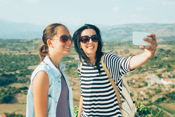 Fototapeta na wymiar Mother and daughter photographing, taking a selfie on mountain peak, whilst resting