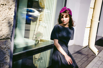 Beautiful woman in a dark stylish dress strolls along the street, near boutiques. Portrait of a fashionable girl