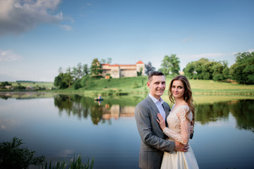 Beautiful newlyweds pose before an old castle on green grass