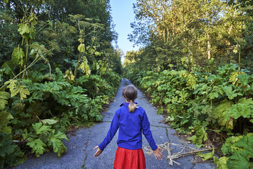 Teen girl standing on the road overgrown by high hogweed