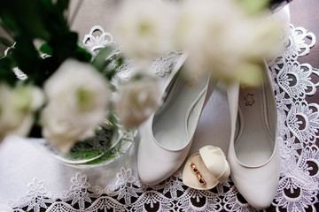 White wedding shoes stand on a table with wedding rings
