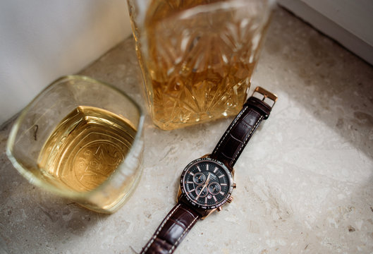 Watch with leather bracelet lies before glasses with whisky