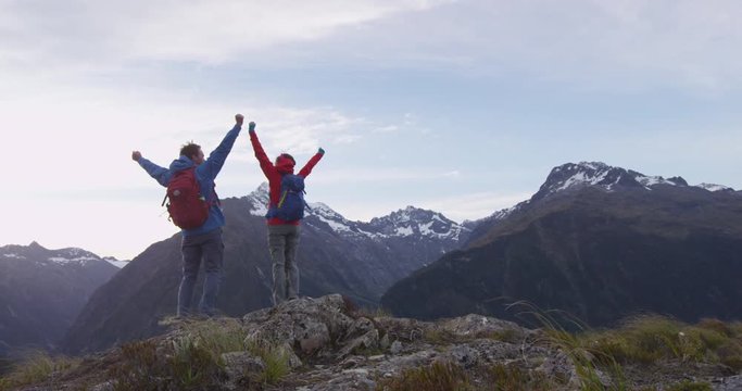 Adventure. Happy hiking couple standing with arms outstretched against mountains at Fiordland National Park. Hikers with backpacks at Routeburn track on vacation in New Zealand, SLOW MOTION.