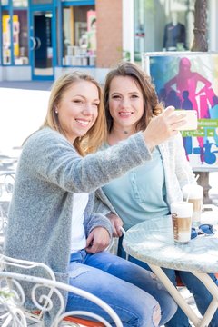 Two friends walk through the city and drink Cappuccino. Two young women sitting in the Cafe. Communication Warm spring. Summer.