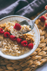 Morning breakfast, oatmeal in milk with raspberries and walnuts on a metal spoon