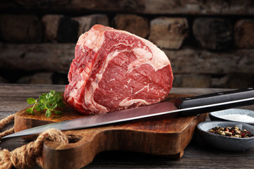 Raw fresh meat Ribeye Steak, seasoning and meat fork on dark background