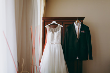 Fototapeta na wymiar Wedding dress of the bride and groom's suit hang in the room
