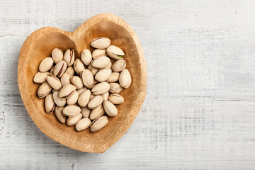 Pistachio nuts in heart shaped wooden bowl on wooden background