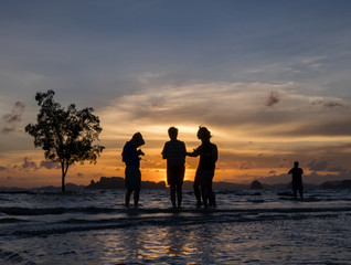 Silhoettes of people enjoying the sunset on the beach in tropical country, Krabi, Thailand.