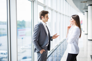 two young businessman and business woman are standing in modern office with panoramic windows.