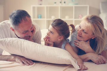 Fototapeta premium Grandmother and grandfather lie together with their granddaughter.