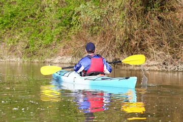 Man in blue kayak in red life jacket kayaking in wild Danube river on biosphere reserve in spring