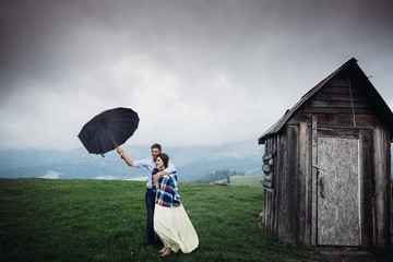 Couple stands under an umbrella on the hill