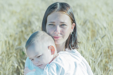 Portrait of a pretty young calm mother holding a small sleepy child in wheat field at sunny summer day