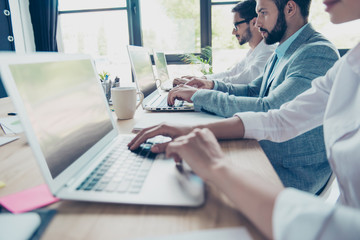 Close up cropped side profile view of three workers sitting in a row busy, typing on their laptops, dressed according to office dress code, focused and concentreted on success