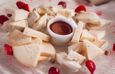 Pieces of cheese and berries served on the plate with red sauce