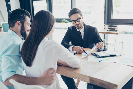 Rear shot of young family, making a deal with lawyer about their business. Men is showing the persentage of a credit of bank, all are well dressed, focused, smiling, sitting in modern office