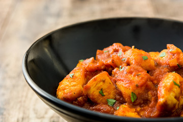 Chicken tikka masala in black bowl on wooden table
