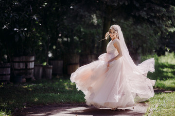 Fototapeta na wymiar Stunning bride whirls on the path under dark green trees