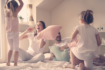 Family having funny pillow fight on bed. Parents spending free time with their daughters. Fight...