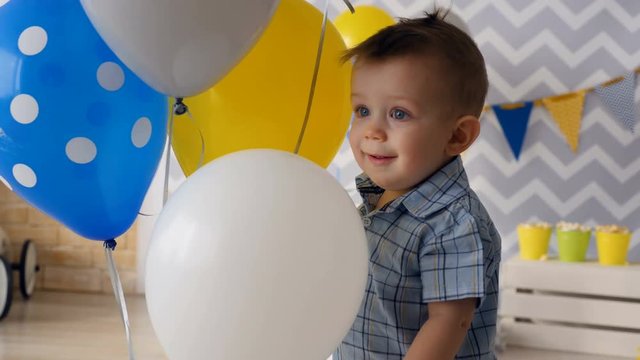 A happy toddler smiles surrounded by balloons. 