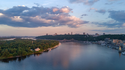 Fototapeta premium Aerial top view of Kiev city from above, hills, pedestrian Park bridge and Dnieper river on sunset, Ukraine 