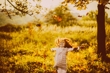 Girl plays with fallen leaves in the evening