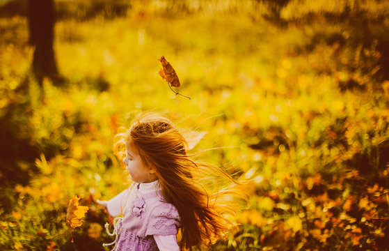 Charming little girl jumps in tall autumn grass