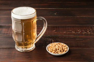 glass of cold frothy lager beer and peanuts plate on wooden table