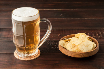glass of cold frothy lager beer and potato chips plate on wooden table