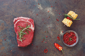 Seasoned raw beef steak with cooking ingredients, on dark rustic stone background. Top view, blank space