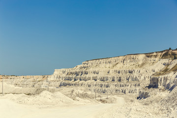White yellow open cast limestone mining quarry at blue sky background