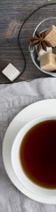 Cup of black tea on wooden table with cane and white sugar cubes, tea spoon and tea strainer. Top view. Wide panoramic. Wide skyscraper.