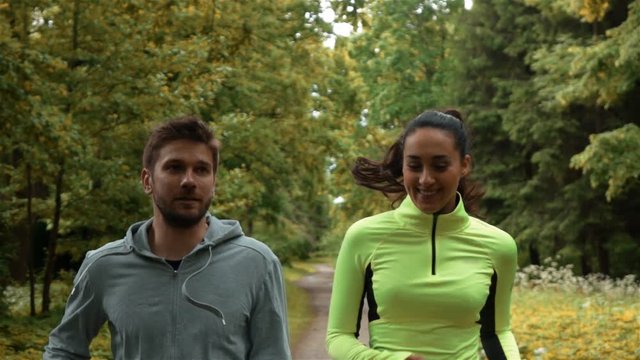 Tracking slow-motion of man and woman communicating and smiling during morning jog. They running at the park. middle shot.