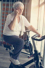 Fototapeta na wymiar Senior woman using smart phone in the gym. Woman talking on the phone. Workout in gym
