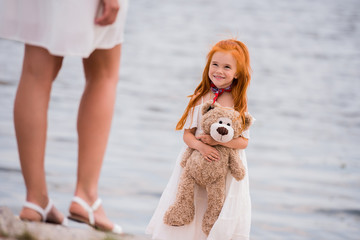 mother and daughter with teddy bear at seashore