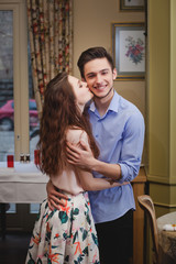 beautiful enamored well-dressed couple standing in cafe and kisses