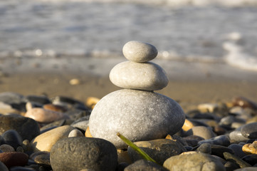 Fototapeta na wymiar White three pebble cairn on the beach, sunlight