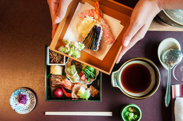 Woman hands open Japanese Bento with grilled seafood and Tempura