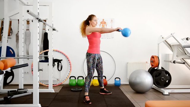 Young beautiful woman sportswoman crouches with a weight in the gym.