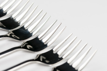 Selective focus closeup macro metal shiny forks lined up over white background